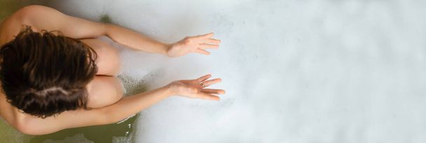 A woman is taking a bubble bath. View from above. Banner, place for text. Relaxation, spa concept. - Фото, изображение