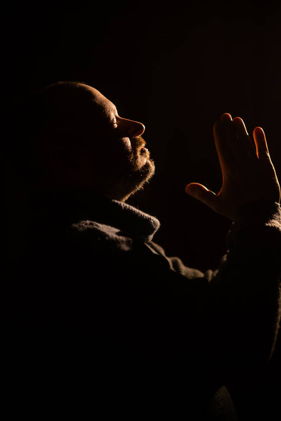Silhouette of a man in prayer. The man folded his hands in communion with God. Dark background. - Φωτογραφία, εικόνα