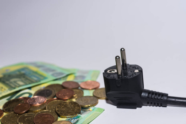 energy consumption and increase in electricity prices euro bills and coins with a power plug on gray background detail view - Photo, Image