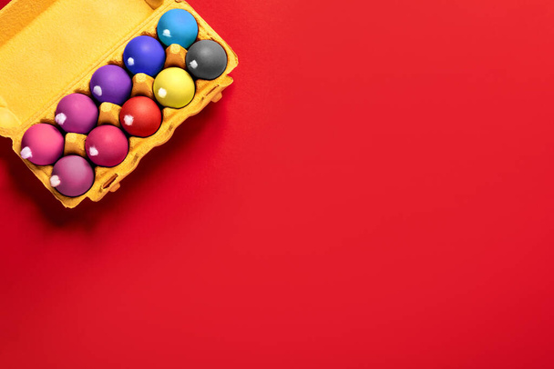 Package of ten chicken eggs with fluffy white tails like Easter bunnies painted in various colors on a solid red background with copy space, empty text place. Banner for the religion holiday. Mockup - Φωτογραφία, εικόνα