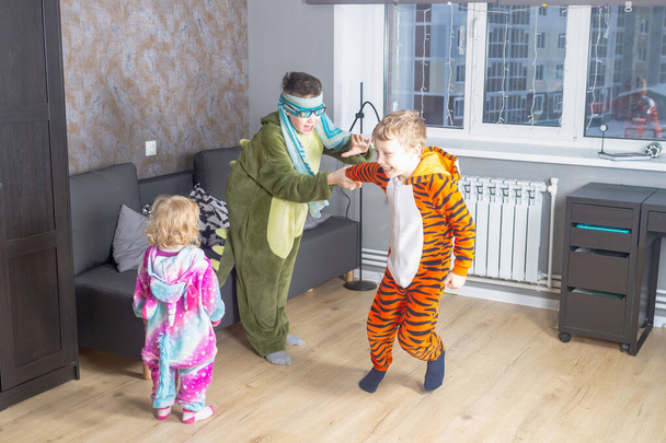Children brothers and sisters in kigurumi pajamas play blind man's buff at home. - 写真・画像