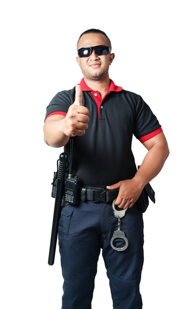 黒の眼鏡をかけた警備員が真っすぐ立ち上がり、親指を立てる。ゴムバトン、手錠、戦術的なベルトが含まれています隔離された白い背景。安全コンセプト. - 写真・画像
