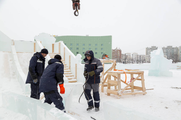 Tres trabajadores cubren el marco de un tobogán de madera con paneles de hielo - Foto, imagen