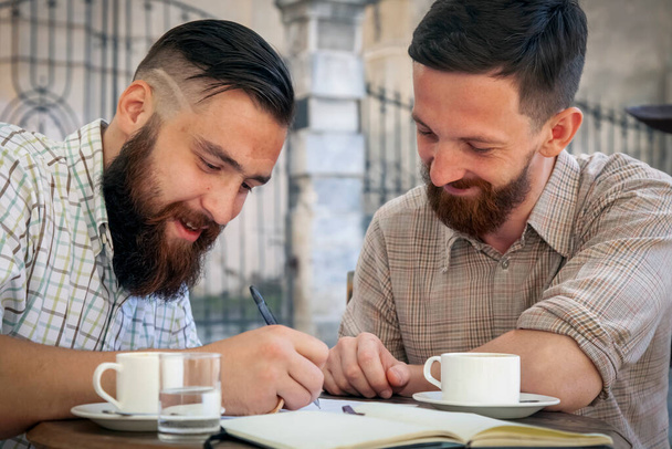 Two hipster freelance businessmen working outdoors on the project and drinking coffee. Concept: happiness, freedom and favorite job. - Foto, Imagem