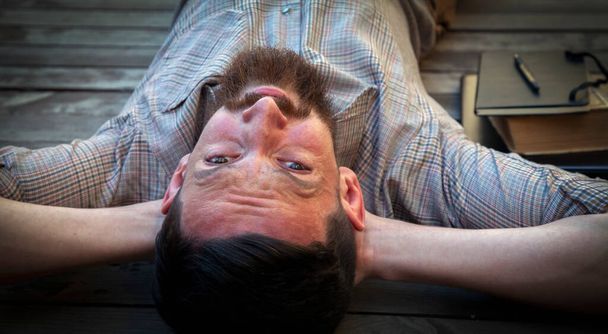 Portrait of hipster businessman lying outdoors on the wooden floor. The man is resting from work.  Selective focus on eyes. Horizontal image. - Photo, image