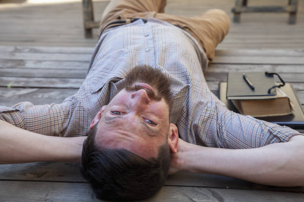 Portrait of hipster businessman lying outdoors on the wooden floor. The man is resting from work.  - Foto, immagini