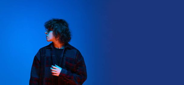 Portrait of young sad man, student posing isolated on blue background in neon light. Concept of emotions, study, education, fashion - Foto, immagini