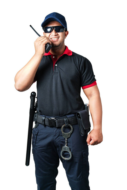 Der Wachmann trägt eine dunkle Brille und einen Hut. Er hält einen Walkie-Talkie mit Gummiknüppeln und Handschellen an einem taktischen Gürtel auf einem isolierten weißen Hintergrund. - Foto, Bild