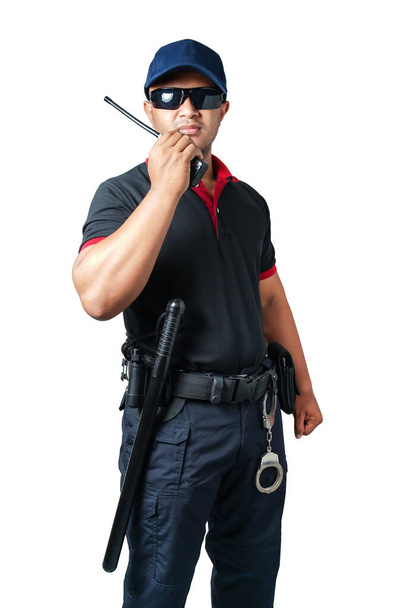 Ochroniarz nosi ciemne okulary i kapelusz. Trzymanie krótkofalówki z gumowymi pałkami w gotowości i kajdanki na pasku taktycznym na izolowanym białym tle Wyeliminuj koncepcję bezpieczeństwa - Zdjęcie, obraz
