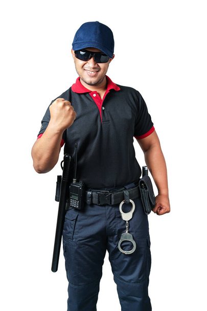 Siyah gözlüklü, şapka takan, yumruklarını mutlu bir şekilde sıkan, taktik kemerinde lastik sopa ve kelepçe olan bir güvenlik görevlisi. izole edilmiş beyaz arkaplan güvenlik kavramını ortadan kaldır - Fotoğraf, Görsel