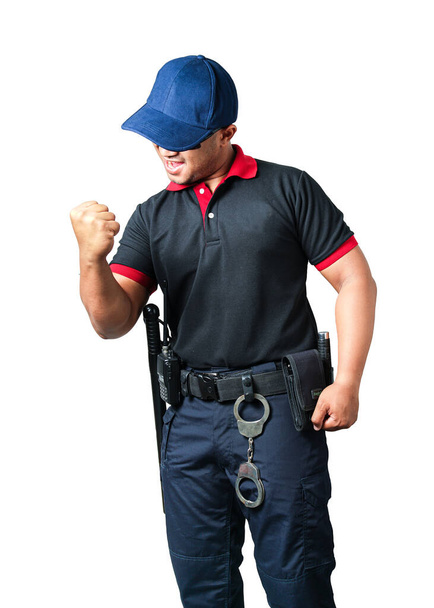 Egy biztonsági őr, aki fekete szemüveget visel, kalapot visel, boldogan szorítja az öklét, gumibotokkal és bilincsekkel a taktikai övén. elszigetelt fehér háttér Távolítsuk el a biztonság fogalmát - Fotó, kép