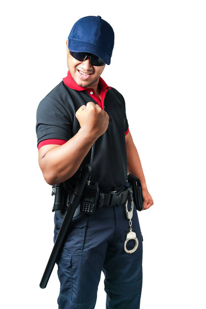 Egy biztonsági őr, aki fekete szemüveget visel, kalapot visel, boldogan szorítja az öklét, gumibotokkal és bilincsekkel a taktikai övén. elszigetelt fehér háttér Távolítsuk el a biztonság fogalmát - Fotó, kép