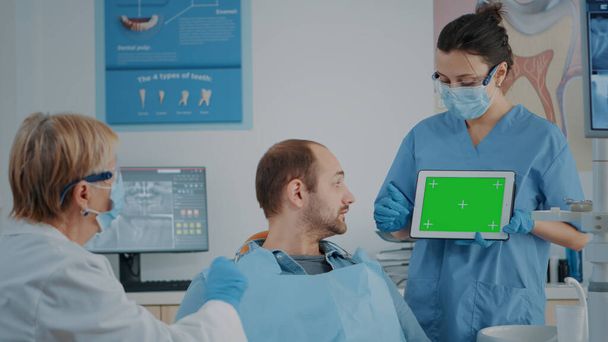 Zespół pacjentów i stomatologów patrzący na tabletkę z zielonym ekranem - Zdjęcie, obraz