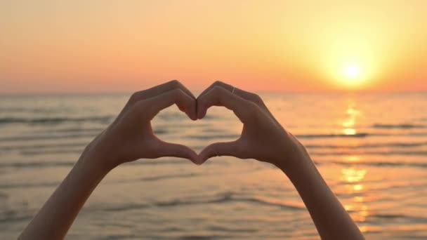 Χέρια στις καρδιές στο φόντο ενός όμορφου χρυσαφένιου ηλιοβασιλέματος πάνω από τη θάλασσα. - Πλάνα, βίντεο