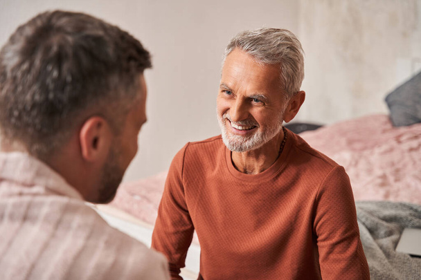 Man remembering something funny with adult son while sitting with each other at home and laughing - Photo, image