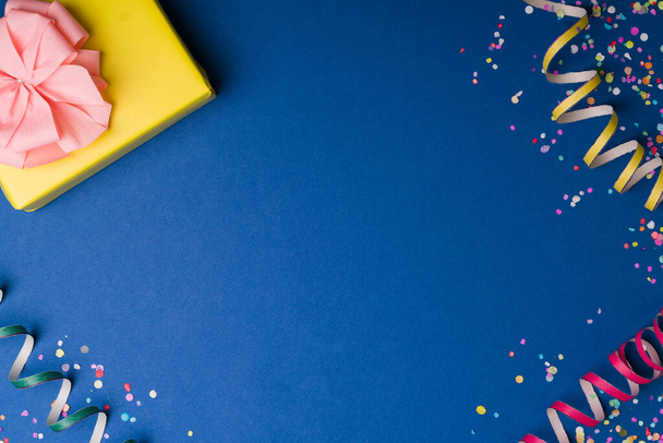 Articles de fête à célébrer. Fond studio bleu avec serpentines colorées, confettis et un cadeau d'anniversaire avec espace de copie - Photo, image