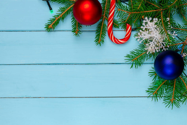 Рождественская спина, земля, зеленые елки ветви, красный и синий шар, конфеты, гирлянда, синие доски - Фото, изображение