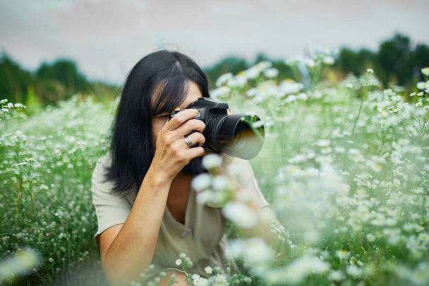 Kadın fotoğrafçının portresi, elinde kamera, elinde dijital kamerayla çiçek tarlası manzarasında fotoğraf çekiyor. Seyahat doğa fotoğrafçılığı, metin için alan, üst görünüm. - Fotoğraf, Görsel