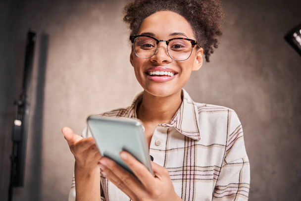Joyful young woman looking at camera, holding smartphone and chatting - Φωτογραφία, εικόνα
