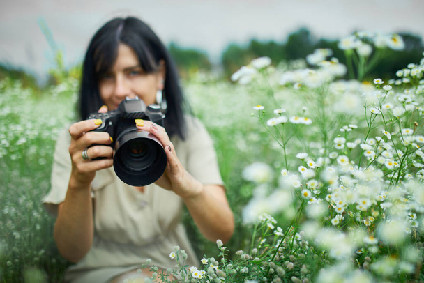 Портрет жінки-фотографа фотографувати на відкритому повітрі на квітковому полі, що тримає камеру, жінка тримає цифрову камеру в руках. Фотографія природи подорожей, простір для тексту, вид зверху
. - Фото, зображення