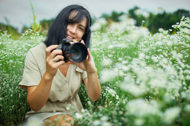 女性写真家の肖像は、屋外の花畑の風景のカメラを保持する上で写真を撮る、女性は彼女の手にデジタルカメラを保持します。旅行の自然写真、テキストのためのスペース、トップビュー. - 写真・画像