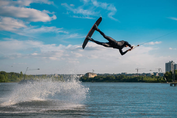 Professional wakeboarder performing jump over water while holding on tow rope - Photo, image