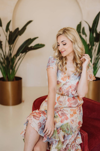 Beautiful happy blonde girl with a shy smile in a summer dress with a floral print. Soft selective focus. - Foto, immagini