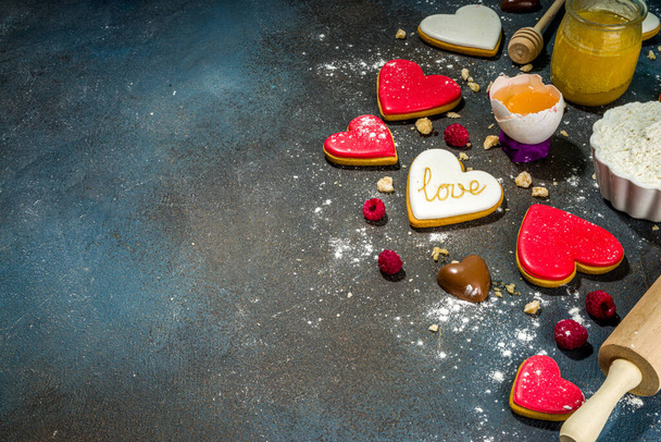 Valentine day sweet cooking background. Baking ingredients and utensils - flour, rolling pin, heart shaped biscuits, eggs. Making cute Valentine`s sweet gift. Top view copy space on dark blue background - Photo, Image