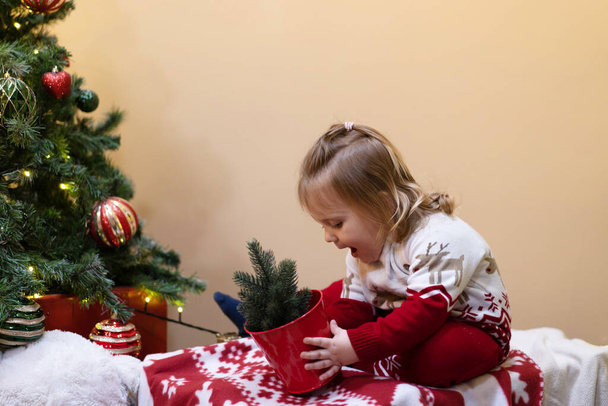  A baby are sitting near the Christmas tree with gifts.  - Foto, Imagen