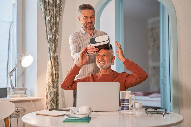Adult son and his senior father with VR goggles at home - Foto, afbeelding