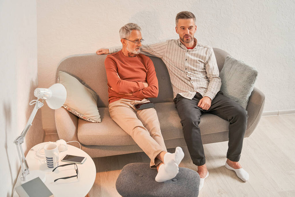 Mature man relaxing with elderly dad while speaking and sharing thoughts on sofa in living room - Foto, immagini