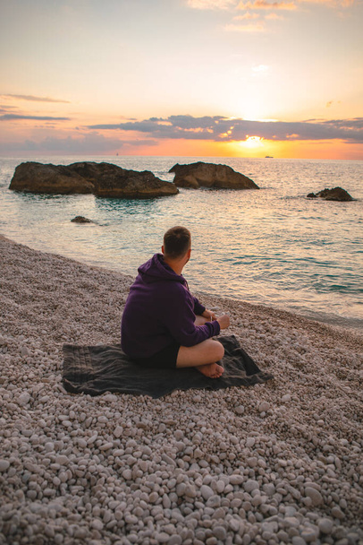 サンセット・ギリシャの休暇を楽しんで海のビーチに座っていた男が - 写真・画像