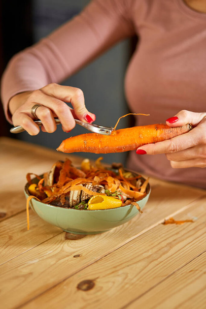 Women scraps peels carrots vegetable peeling, throws in compost bucket, organic composting leftover from kitchen, Compost, recycling, zero waste, Garbage sorting - Photo, Image