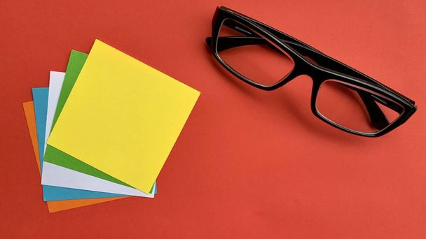 Bovenaanzicht van kleurrijke notitieblokken met bril en rode achtergrond. - Foto, afbeelding
