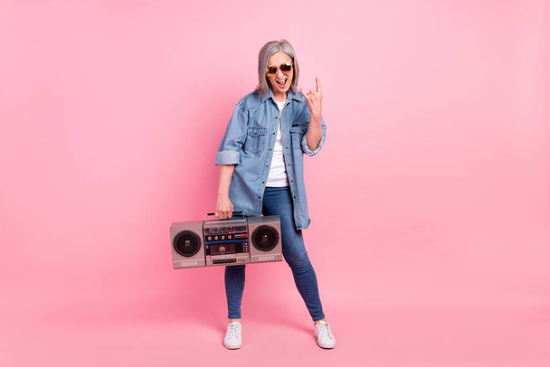 Full body photo of cool aged lady show rock sign hold boom-box wear shirt jeans isolated on pink background - Valokuva, kuva