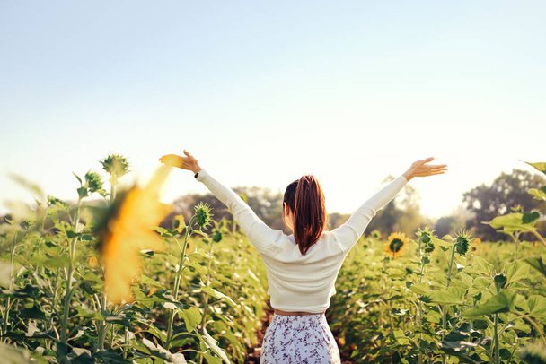 Happy woman standing and open her arms in a sunflower field at sunset. concept of freedom. - 写真・画像