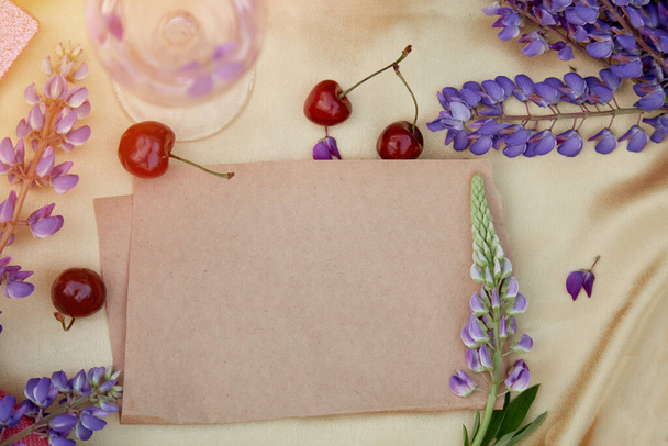 Craft paper mock up. Lupins purple flowers, wine glass, apple and cherry decorations. Summer invitation, birthday card, Mothers day concept. Feminine vibrant background. Natural, wellness closeness - Photo, Image