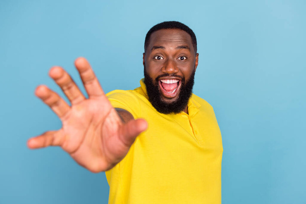 Photo of shocked funny dark skin man wear yellow t-shirt smiling showing palm isolated blue color background - Foto, Imagem