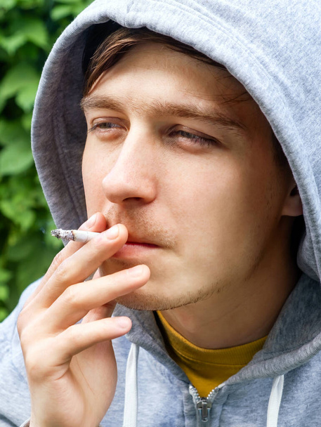 Young Man smoke a Cigarette Portrait on the Green Leaves Background closeup - Fotó, kép