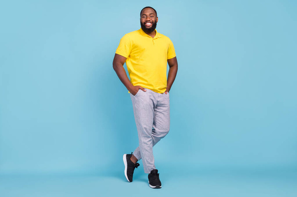 Photo of excited shiny dark skin guy dressed yellow t-shirt smiling arms pockets isolated blue color background - Foto, Bild