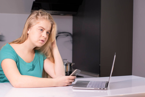 Ernstige jonge blonde vrouw die online van huis studeert tijdens een quarantainevirusuitbraak. Ik werk aan een laptop in haar grijze kamer. Een close-up. Blijf thuis concept. Problemen met werk oplost. Kopieerruimte - Foto, afbeelding