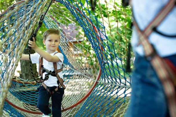 Portrait of a little boy in climbing gear in a rope park, holding a rope with a carbine - Photo, Image
