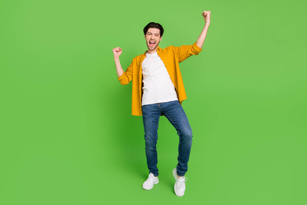 Full size photo of young handsome cheerful screaming guy raise fists winner triumphant isolated on green color background - Photo, Image