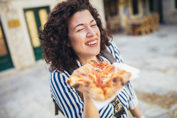 Beautiful young tourist woman eating a slice of pizza outdoor - Фото, изображение