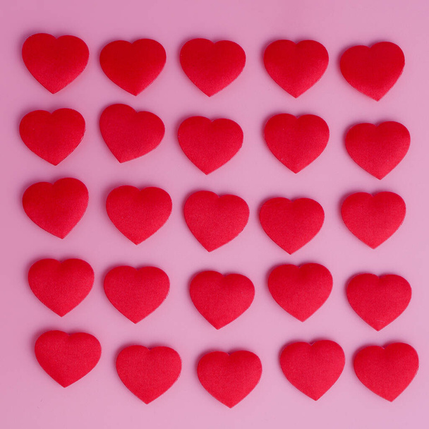 Dwadzieścia pięć małych czerwonych serc tkaniny na różowym tle w kształcie kwadratu. Przypomina magiczne cukierki miłosne. Romantyczne i stylowe miękkie różowe tło. - Zdjęcie, obraz