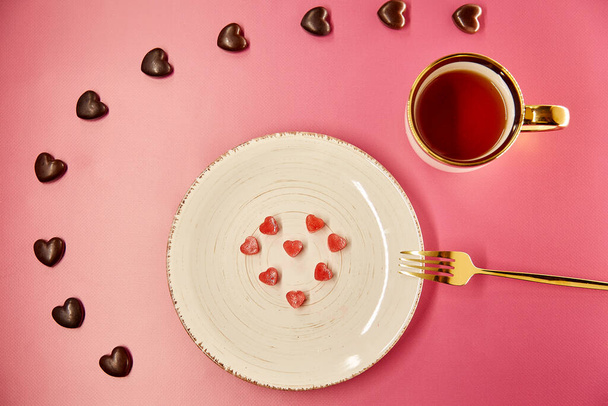 フォークで白いプレートの上にかわいい凍結氷の心。チョコレートの心のお菓子。創造的なロマンチックなディナー、バレンタインデーのコンセプト。ピンクのグラデーションの背景。トップ表示 - 写真・画像