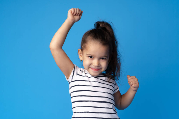 Little cute girl showing her strength on blue background - Фото, изображение