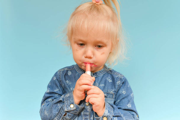 A small child found cosmetics from her mother and paint her lips with lipstick. - Fotoğraf, Görsel