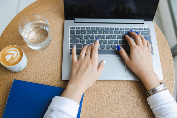 Vista de cerca de las manos femeninas escribiendo en un ordenador portátil. Mujer de negocios trabajando en una mesa en un café - Foto, imagen