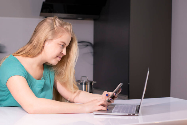 Jeune femme d'affaires en vert avec smartphone. Sur le bureau se trouve un ordinateur portable. Fille travaillant, apprenant en ligne. Médias sociaux, réseau. Marketing en ligne, éducation. - Photo, image